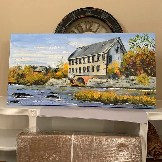 Landscape painting of an old mill building near a river with trees showing fall colors under a partly cloudy sky.