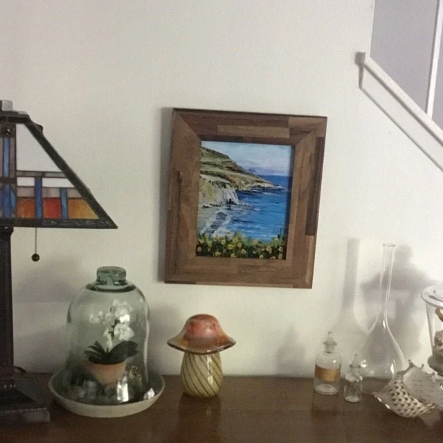 Interior wall with framed landscape painting, glass jar with plant, decorative objects, and part of a stained glass lamp.