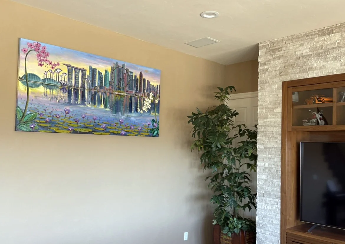 A living room wall with a colorful cityscape painting, a tall green plant in a pot, a built-in wooden entertainment center with a TV, and a textured white brick wall.