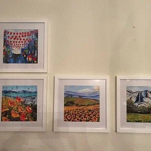 Four landscape paintings framed and hung on a beige wall