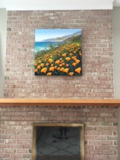 Colorful landscape painting of a coastal scene with orange flowers in the foreground, blue water, and distant hills on a brick wall.