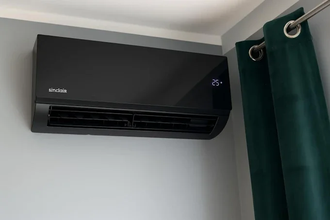 Wall-mounted black air conditioner with digital display showing 25 degrees, next to green curtains on a gray wall.