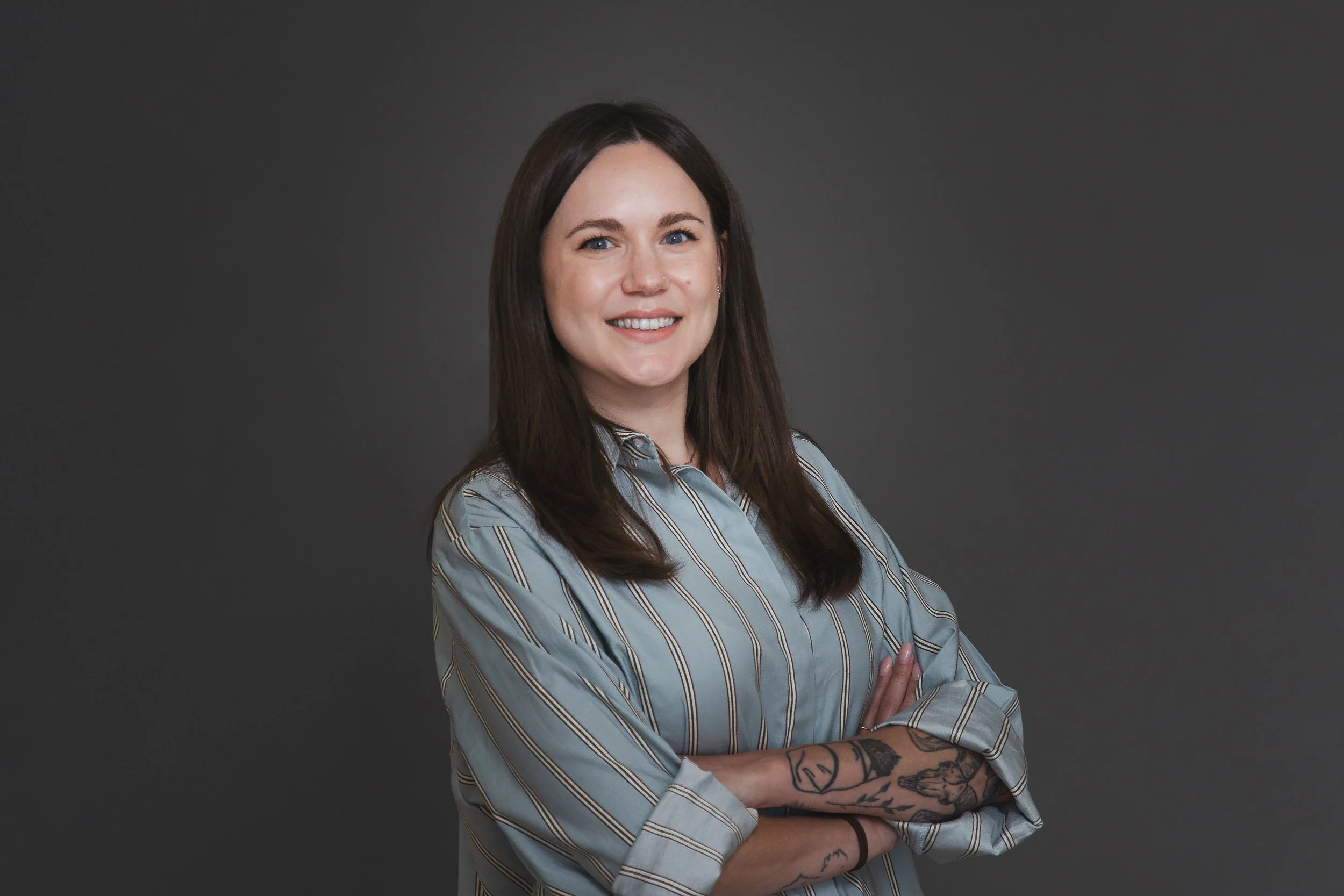 Amber Hewitt smiling with arms crossed, wearing a blue striped shirt.