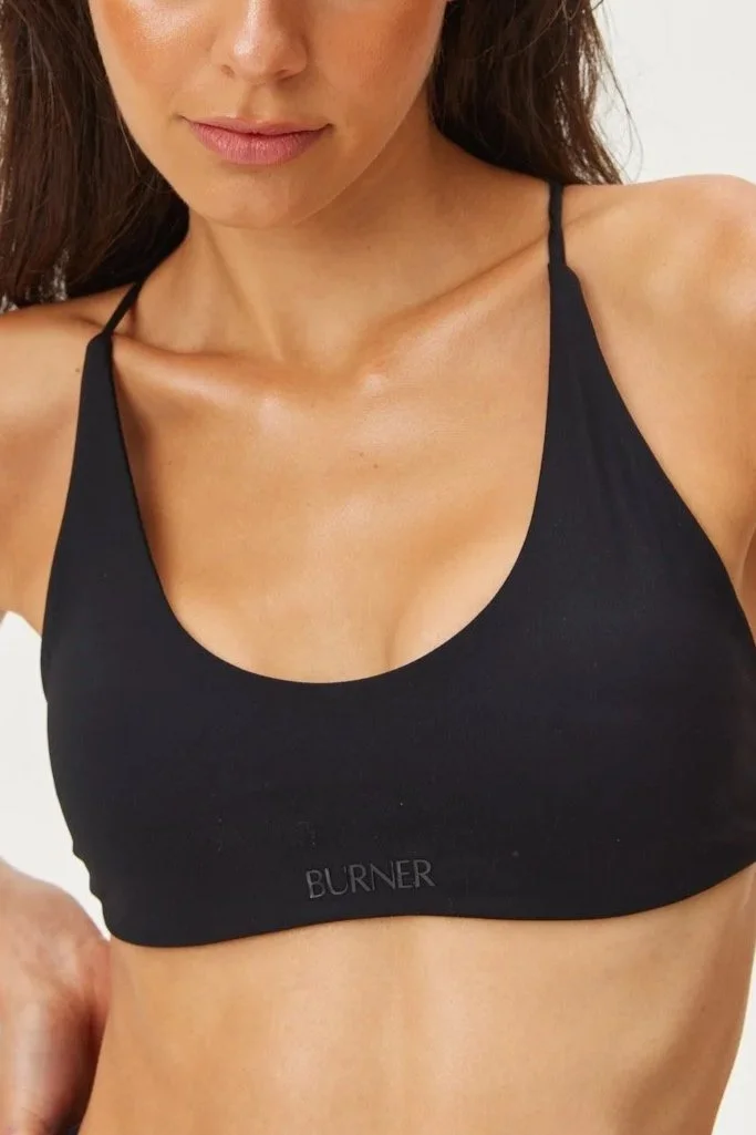 Close-up of a woman's upper body wearing a black sports bra with the word 'BURNER' on it, showing her collarbone, shoulders, and partial face.