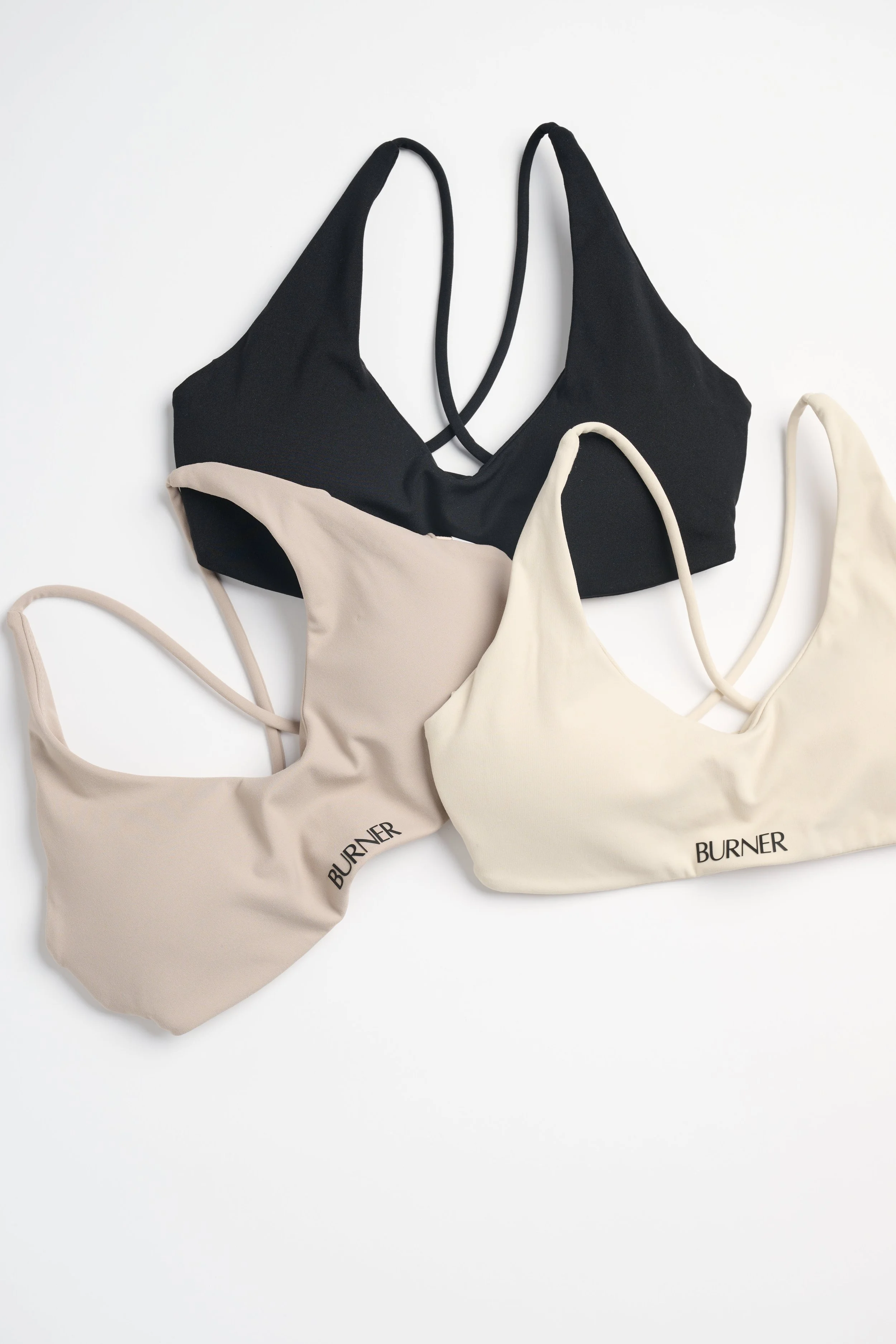 Three beige and one black sports bras with straps, laid out on a white background, with the word "BURNER" printed on the beige bras.