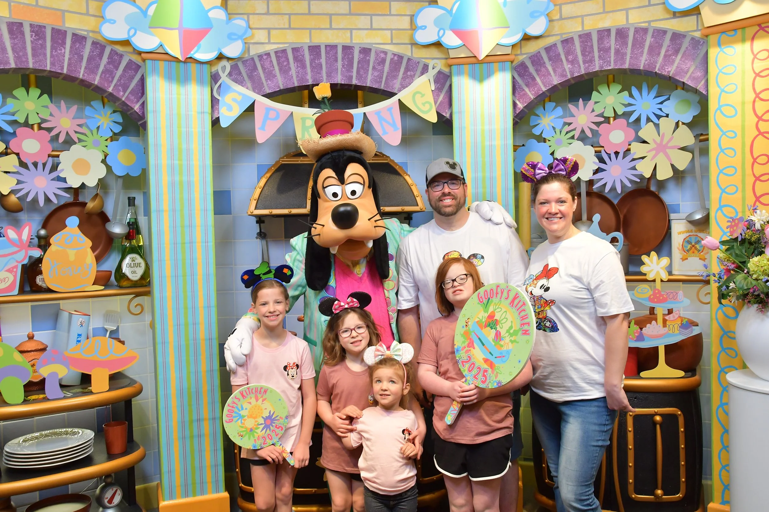 Turnwalds at Goofy's Kitchen, all posing in front of a colorful spring-themed backdrop with flowers and kitchen decorations.