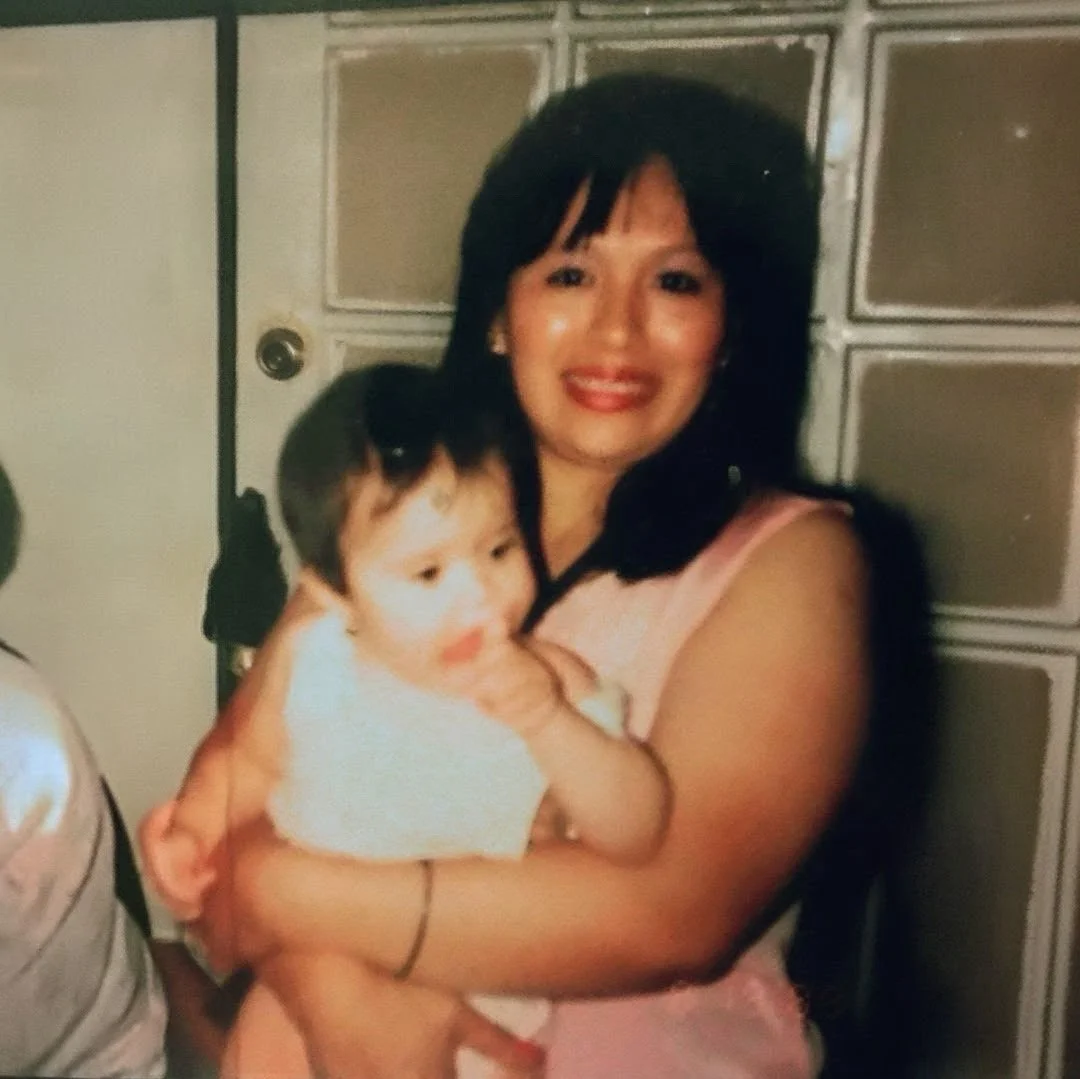 A woman with black hair holding a young child with dark hair in front of a metal locker or cabinet.