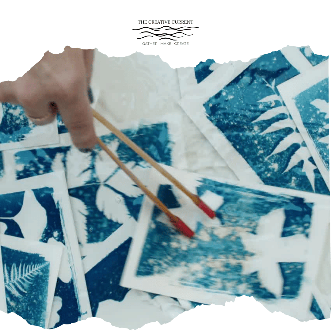 A hand holding chopsticks over a collection of cyanotype prints featuring botanical images.