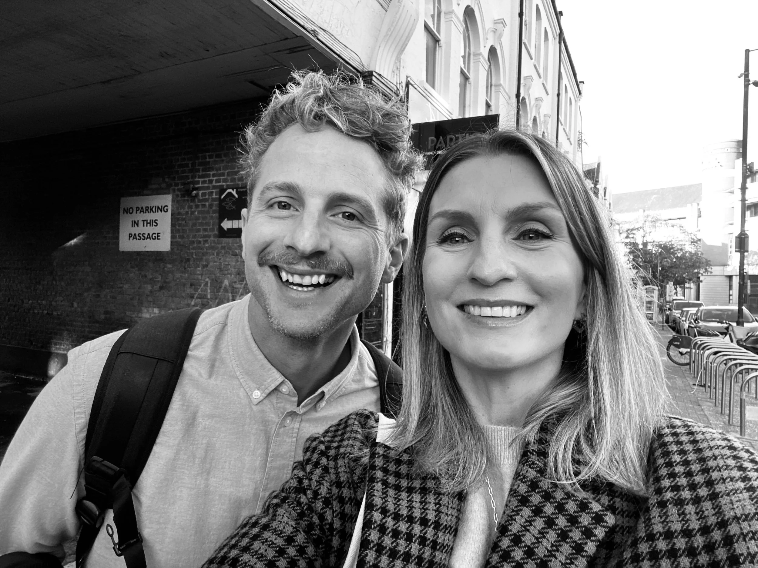 A black-and-white photo of Rik Turner and Hannah Harris taking a selfie together outdoors on a London street.