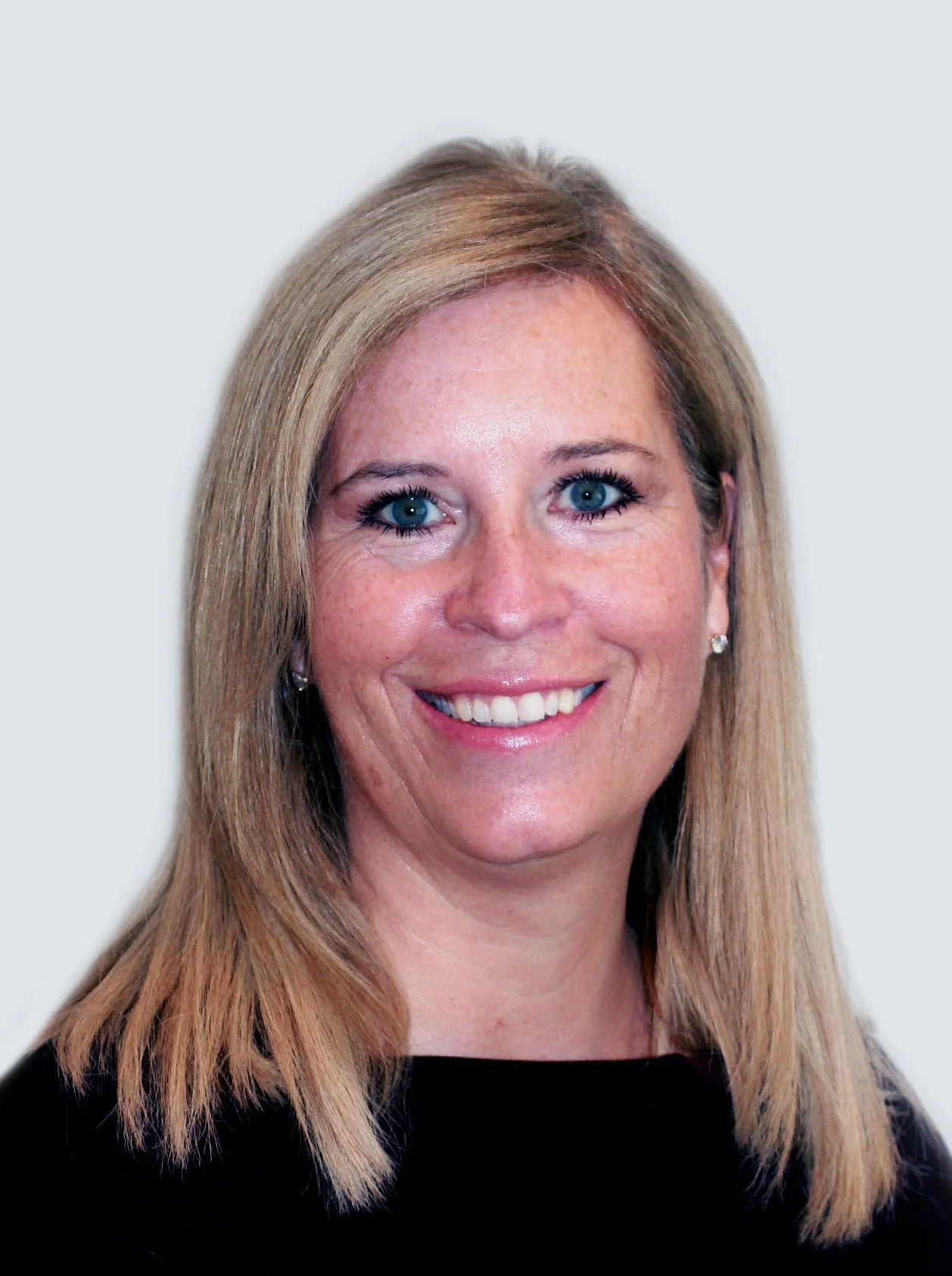 A woman with blonde hair, blue eyes, wearing earrings and smiling, against a plain light background.