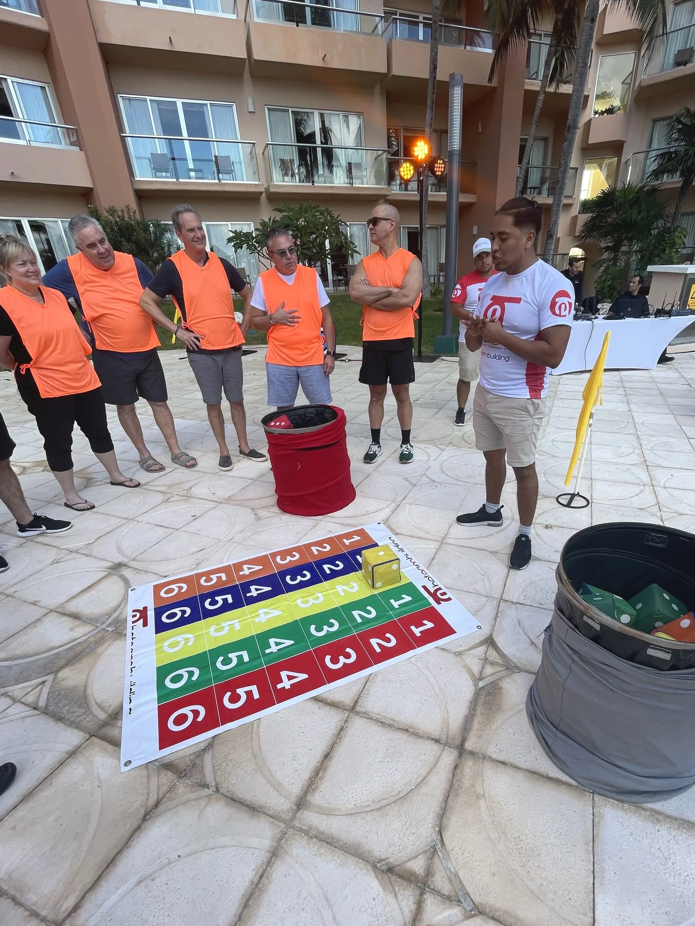 Team building activity for SKO Leadership summit - various teams setting up for a mini version of The Amazing Race. Instructor explaining game rules while team stands surround listening. 