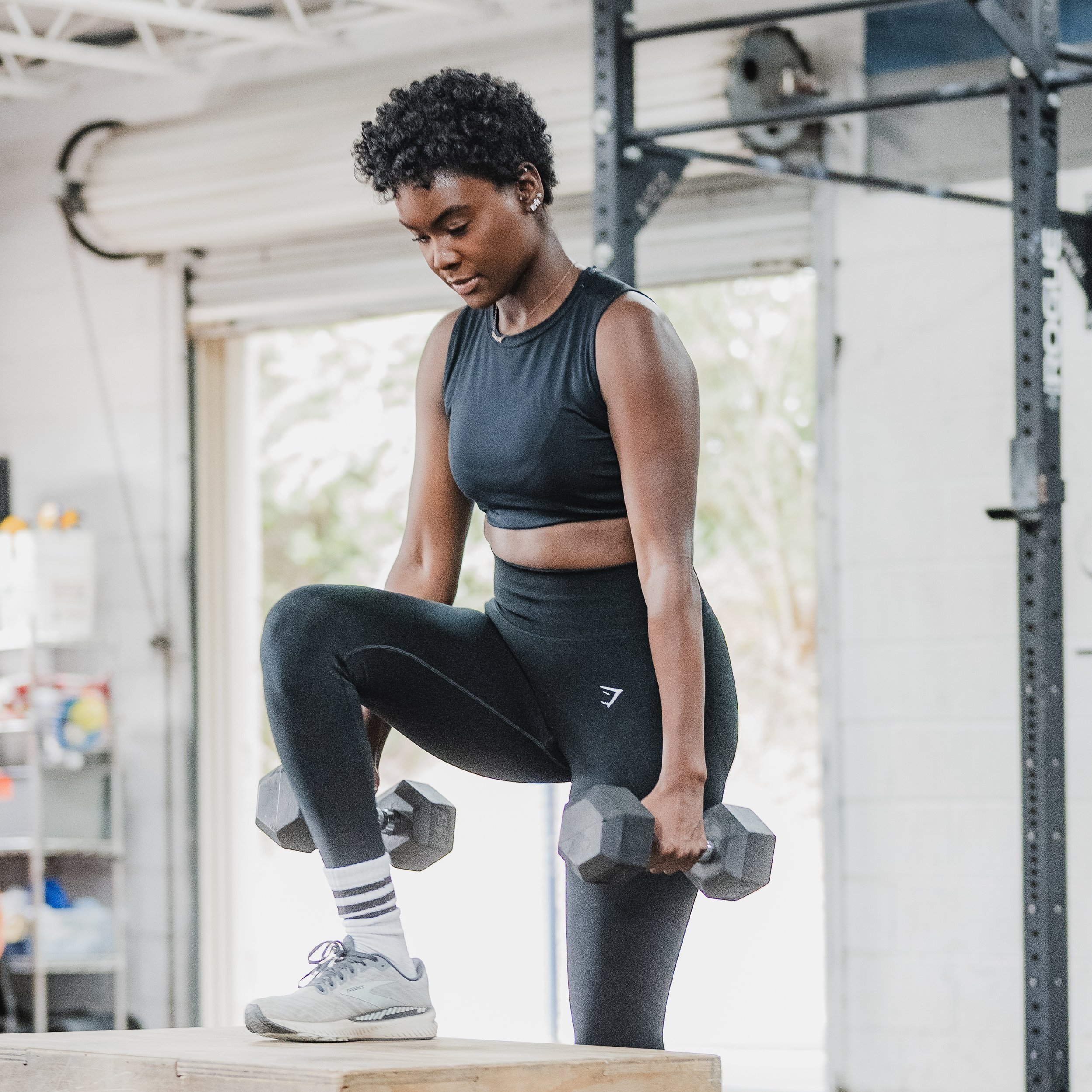 A woman wearing workout clothes lifting dumbbells during a workout session in a gym.