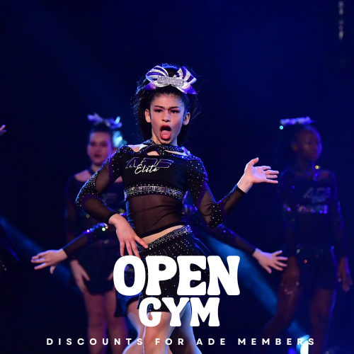 Young girl in a black and purple cheerleading uniform performing on stage with other cheerleaders in the background, lit with purple and blue stage lights. ADE ELITE ATHLETICS OPEN GYM