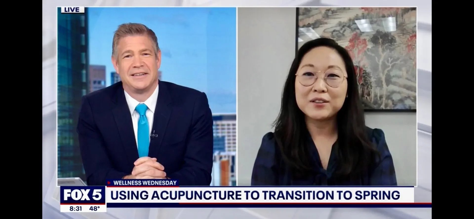 Television news interview showing a male news anchor on the left and a female guest on the right, discussing acupuncture as a method to transition to spring, with station branding and a cityscape background visible.