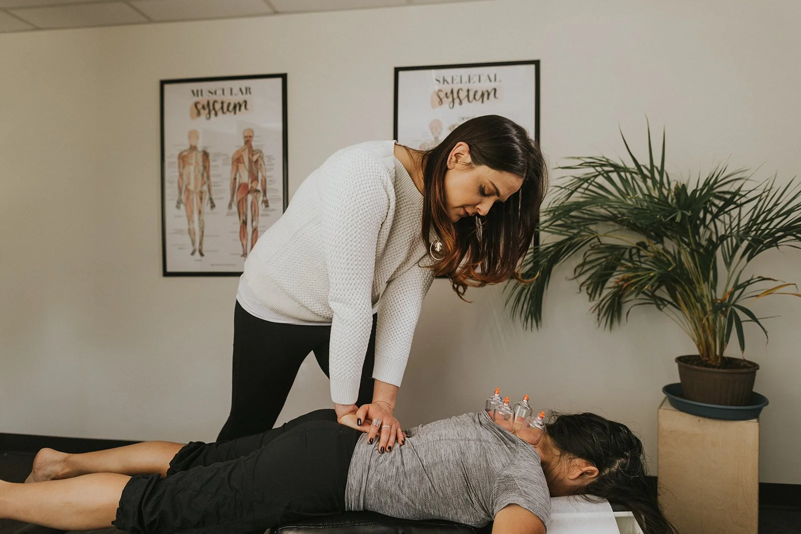 Female chiropractor performing an adjustment on a female patient lying face down on a chiropractic table in a medical office.