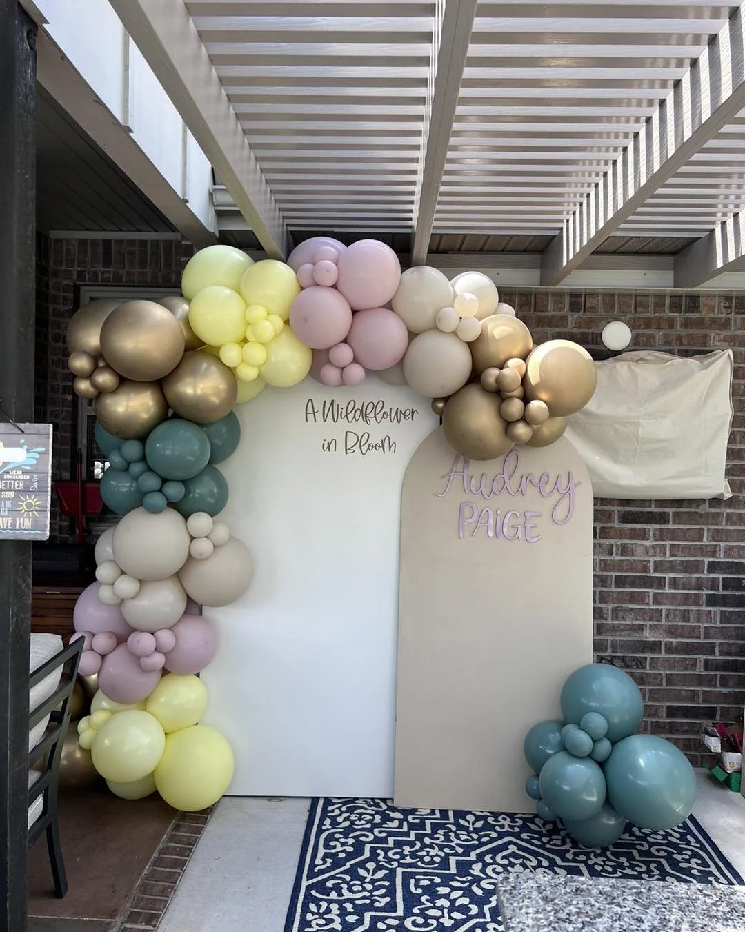 Colorful balloon arch with pink, yellow, green, and orange balloons, decorated with flowers, placed at the entrance of a brick building.