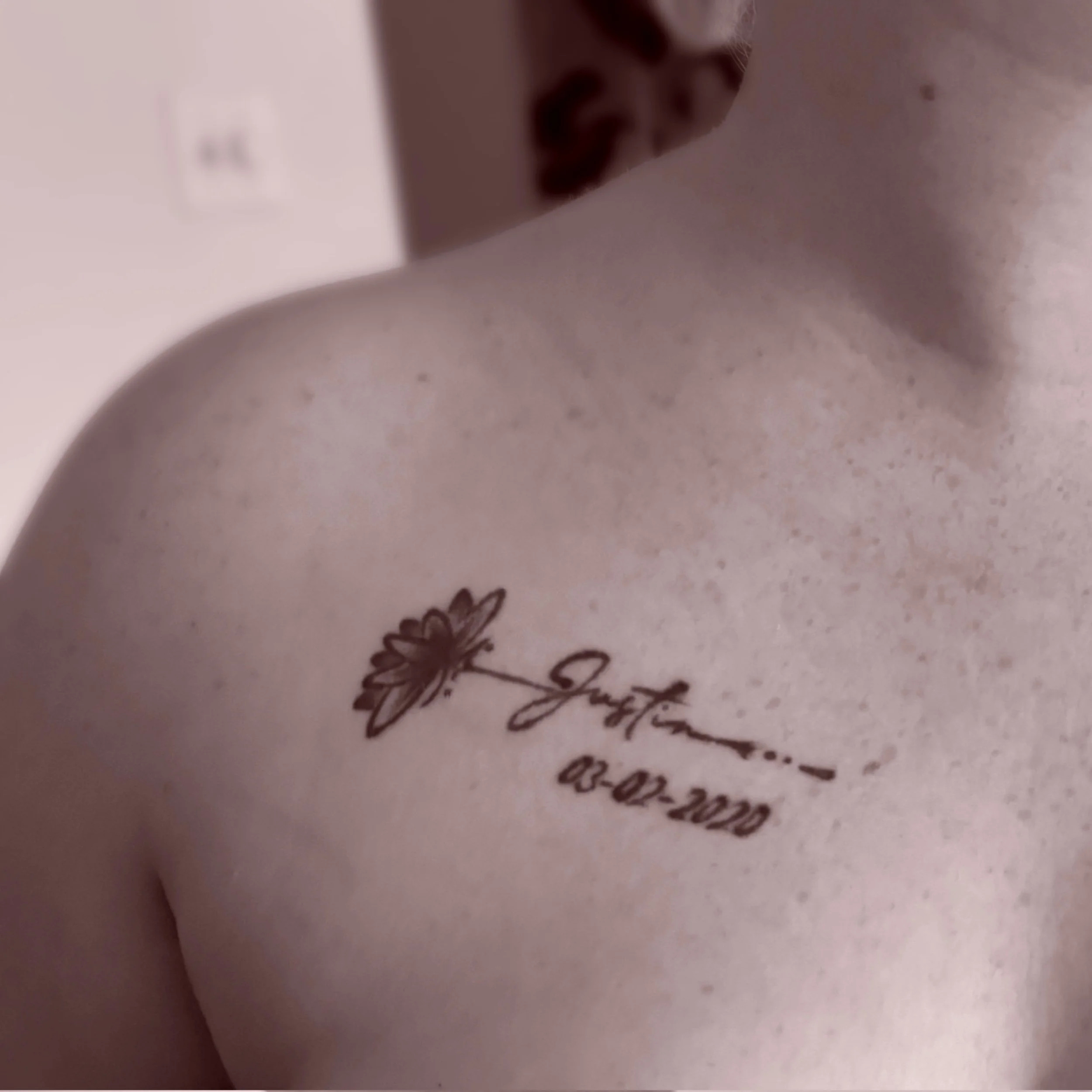 A tattoo on a person's shoulder of a daisy flower, with the name 'Jersey' and the date '08-02-2020' written underneath.