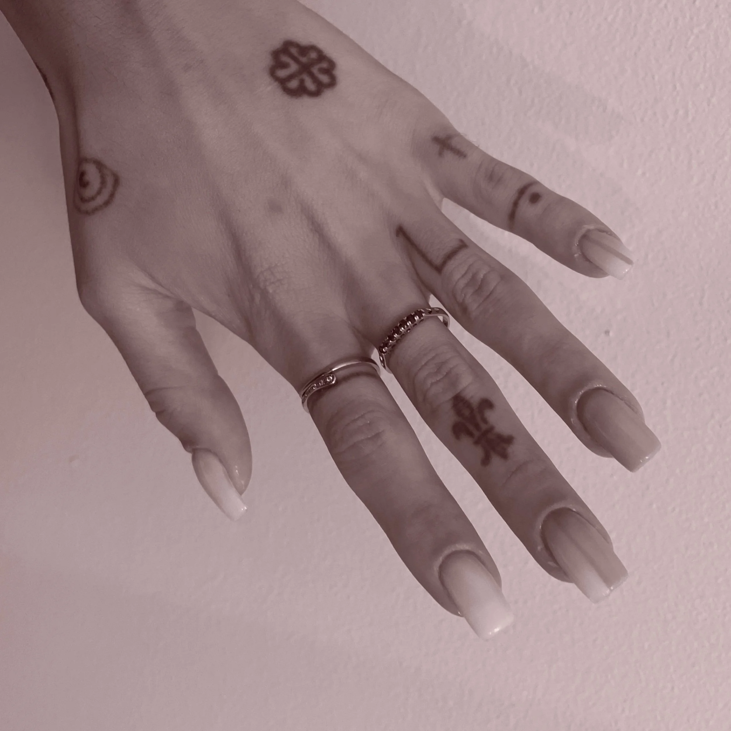Close-up of a hand with tattoos and rings, against a light pink background.