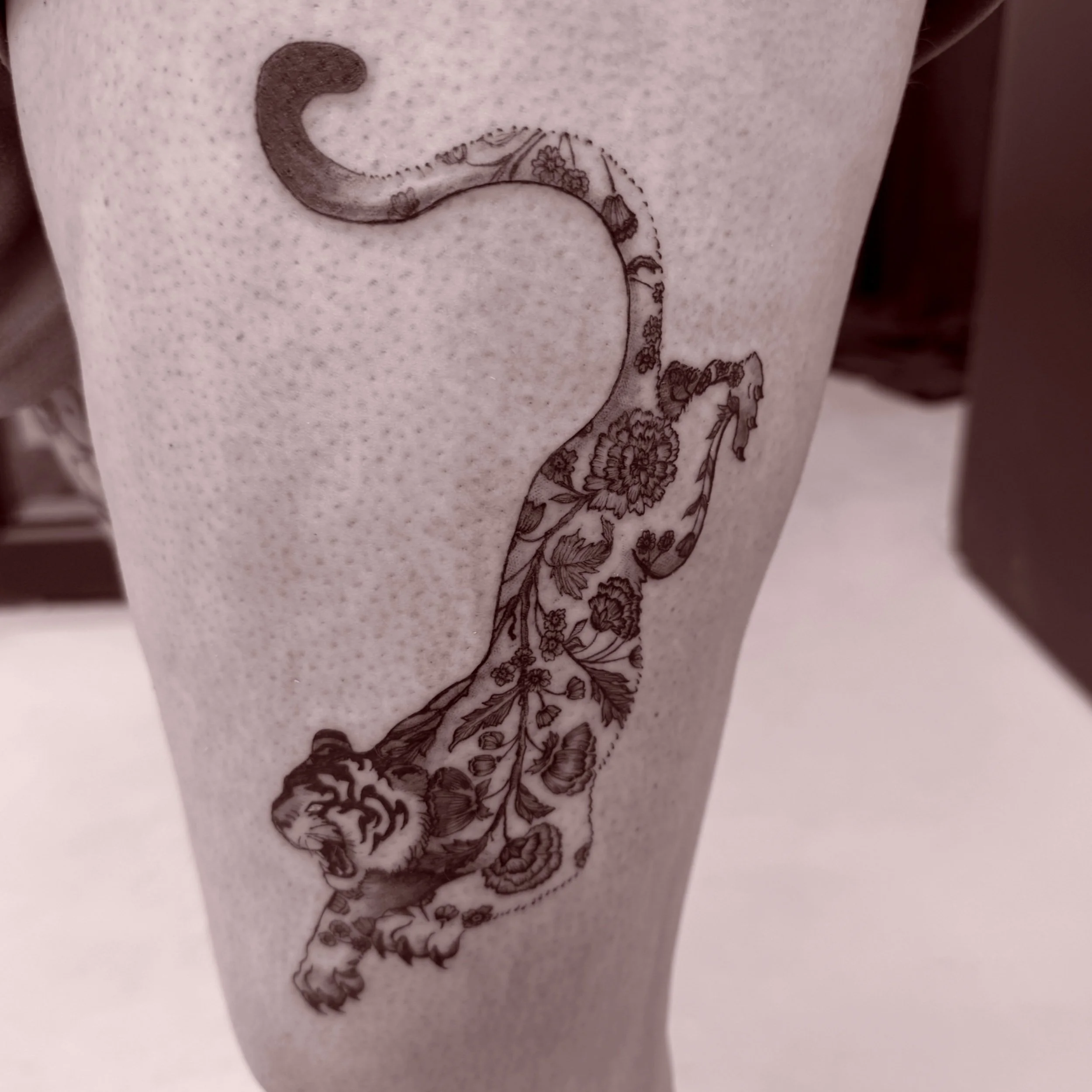 A decorative coffee cup with a floral and tiger design in black ink.