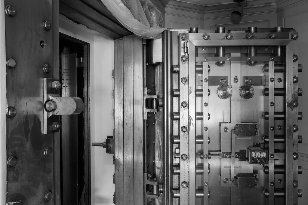 Black and white photo of a large industrial safe with multiple locking mechanisms, gears, and bolts.