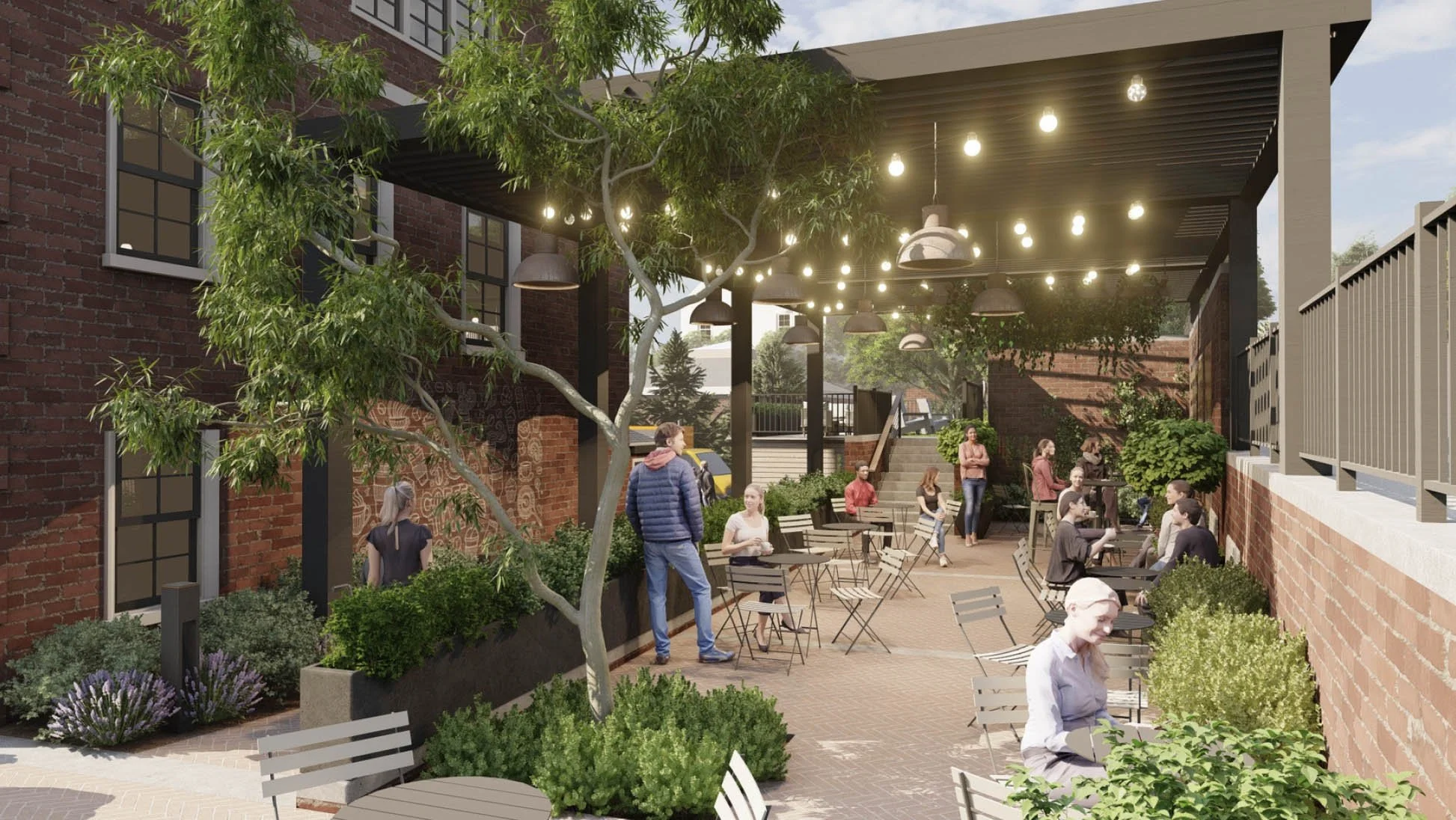 People gather in an outdoor patio with brick walls and metal patio furniture. Trees and greenery surround the area, which has a covered section overhead with hanging lights. Multiple individuals are seated at tables, chatting, while others stand or walk around.