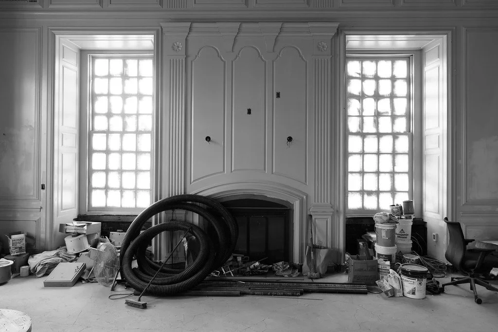 Room under renovation with large windows, construction materials, hoses, and an office chair.