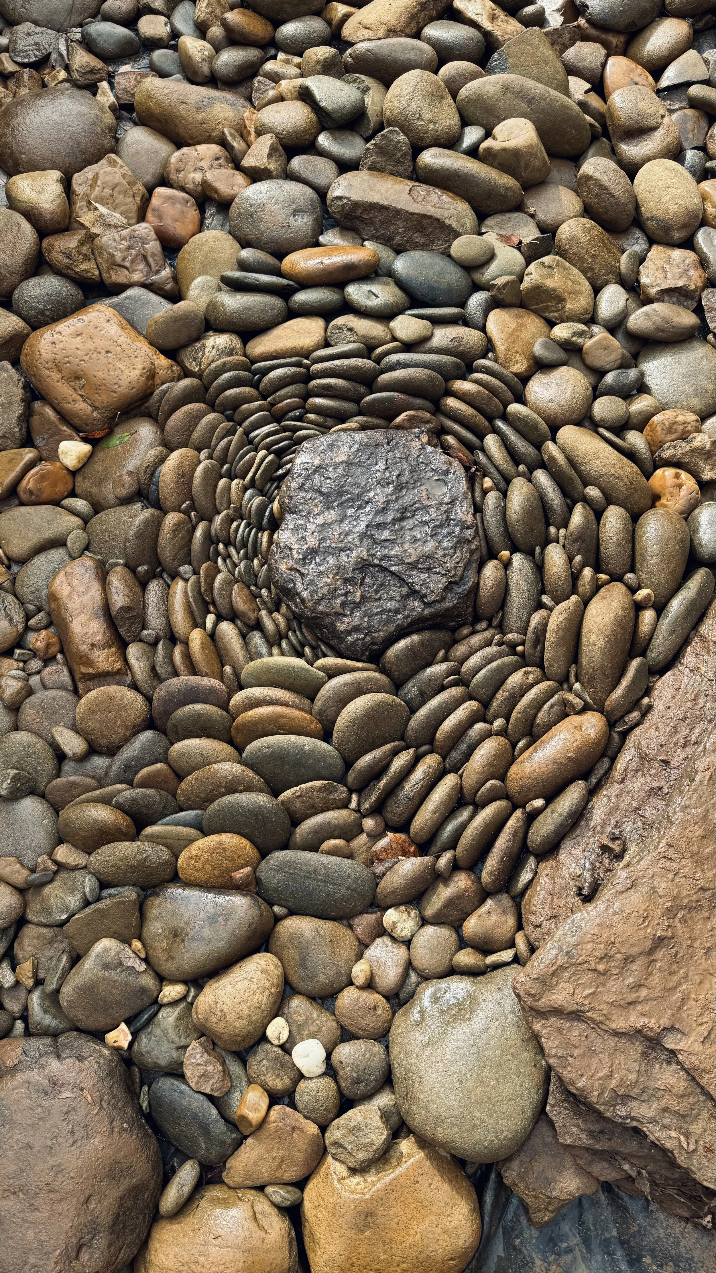 A spiral pattern made with small, smooth river stones around a large central rock.
