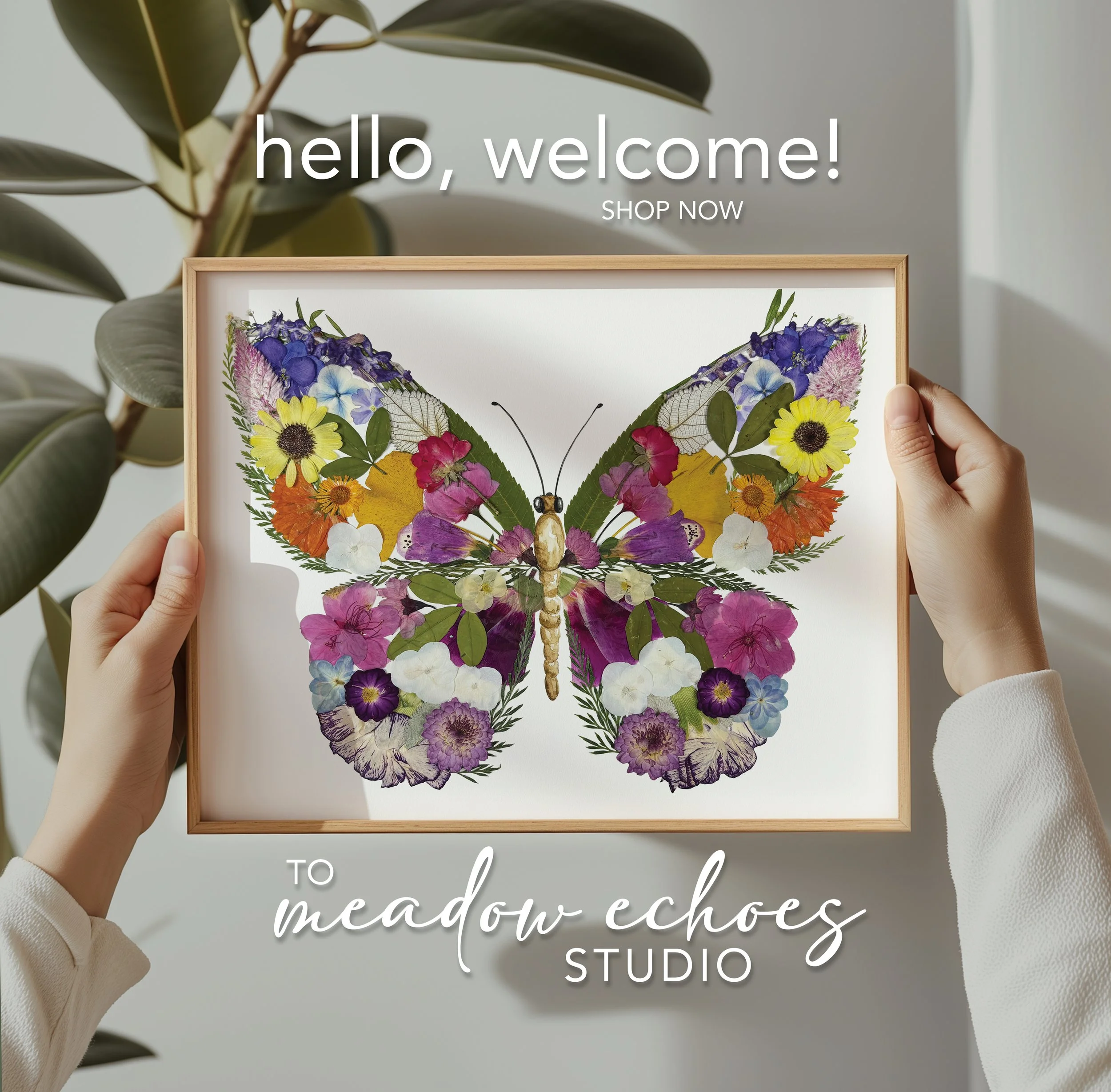 Framed artwork of a butterfly made from colorful pressed flowers, held by two hands against a background of green leaves.