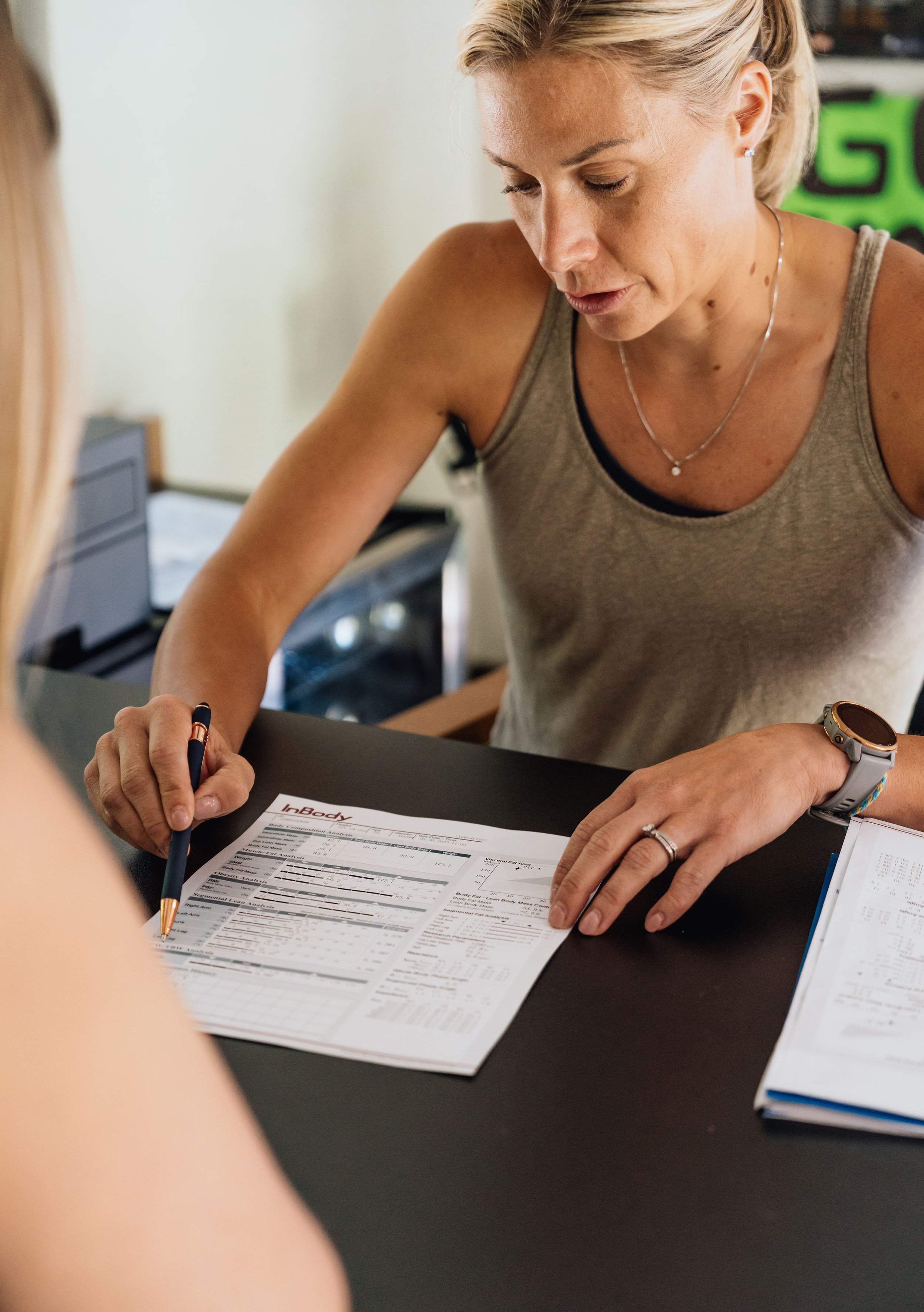 Woman reviewing a health report or form at a desk with a pen in her hand and a smartwatch on her wrist.
