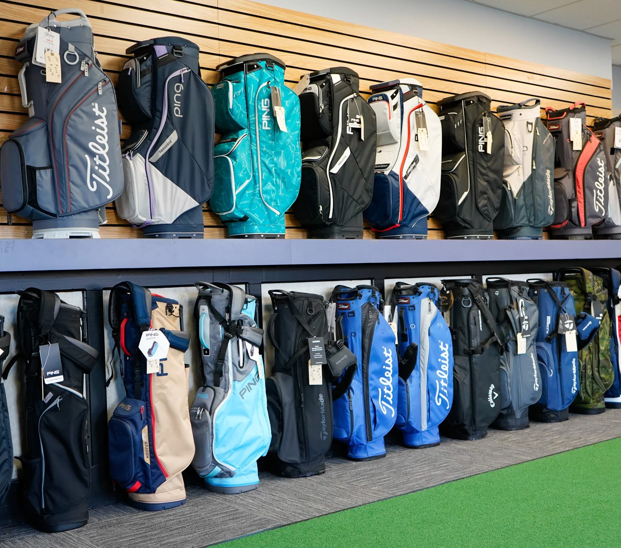 Display of golf bags on shelves in a retail store, showcasing various brands and colors.