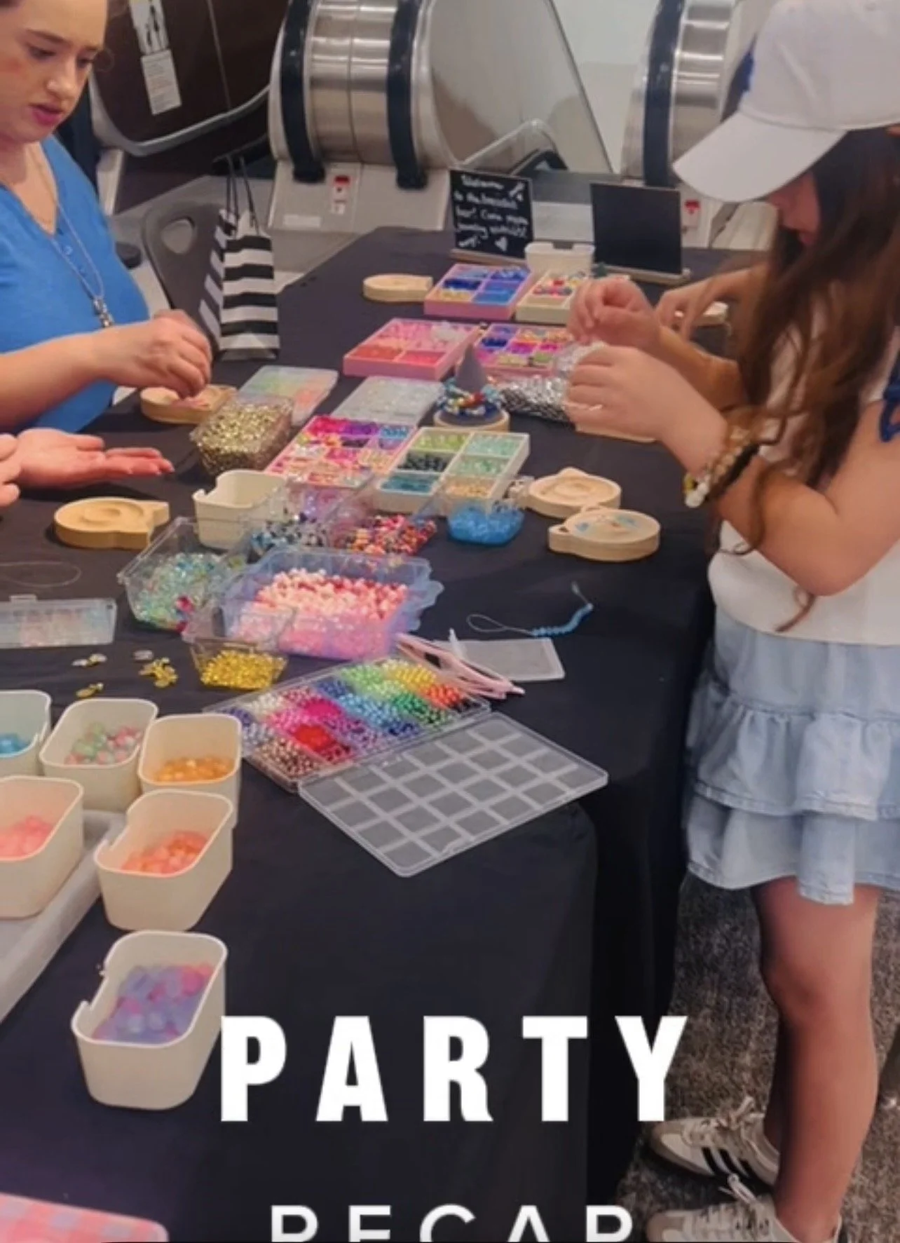 People assembling colorful beaded jewelry at a party table with various beads, containers, and jewelry-making supplies.
