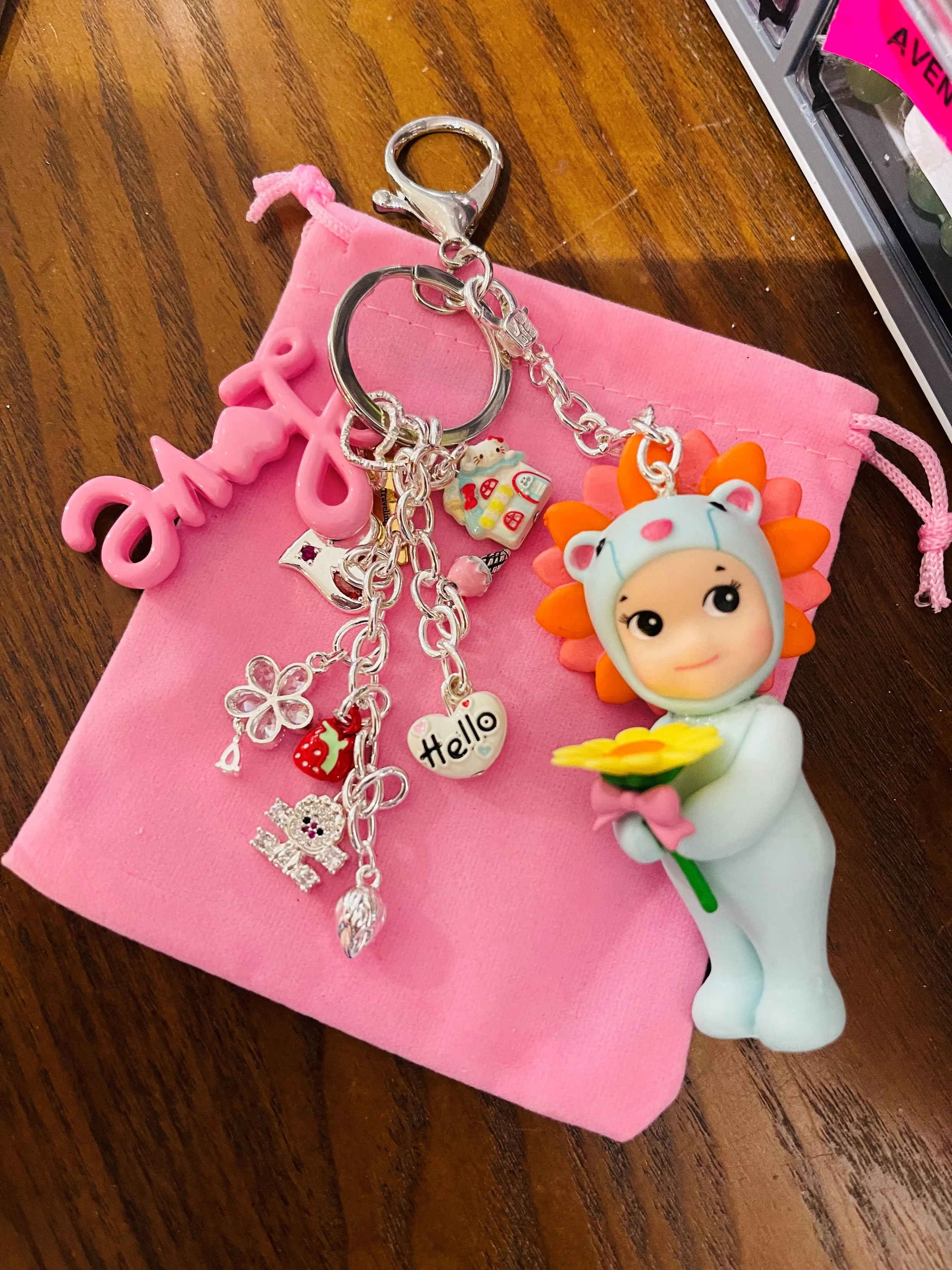 Jonny Angel Keychain with charms, a pink drawstring pouch, and a figure of a child in a lion costume holding a flower, all on a wooden surface.