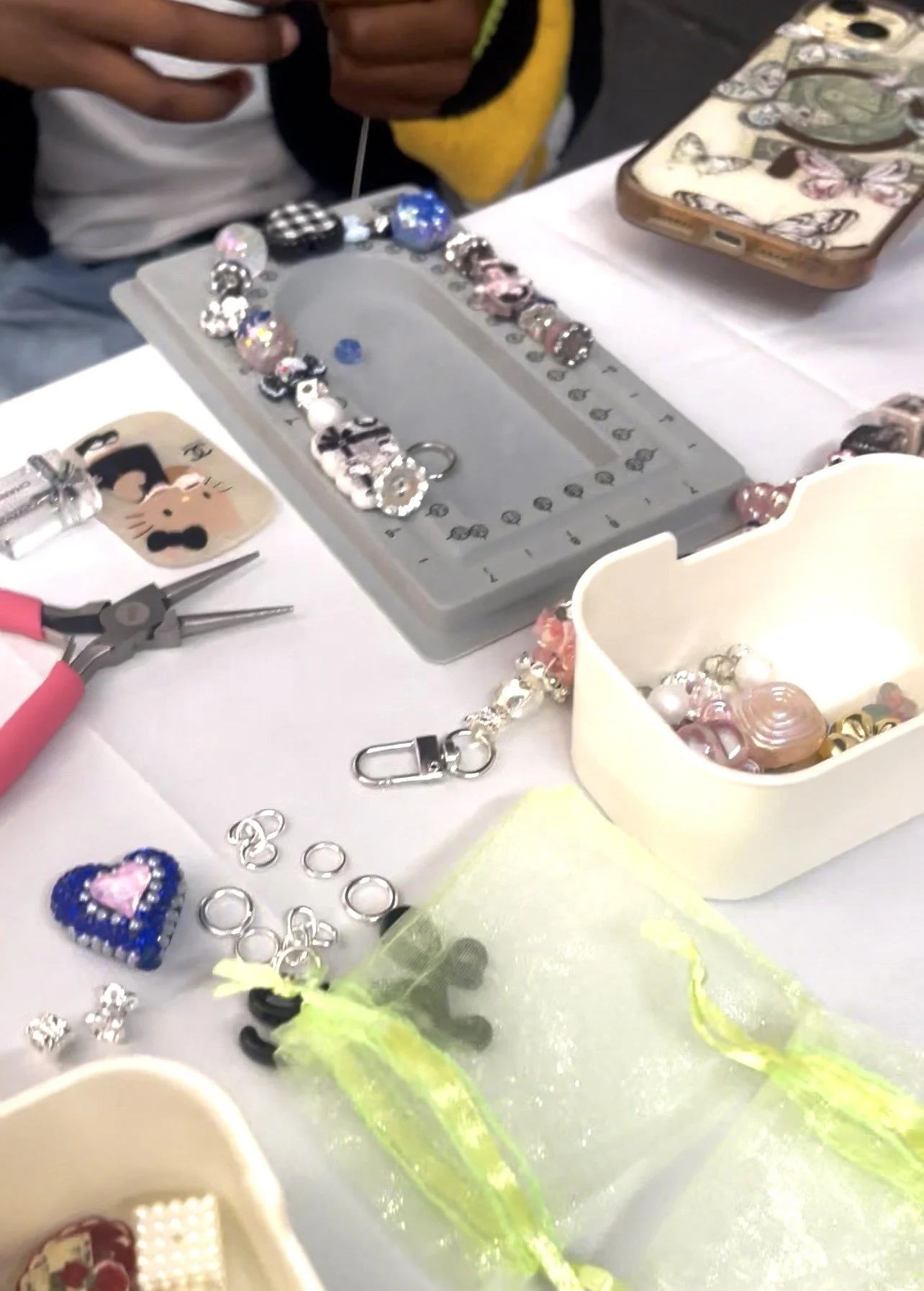 Close-up of a jewelry-making workspace with beads, charms, pliers, and a partially finished bracelet.