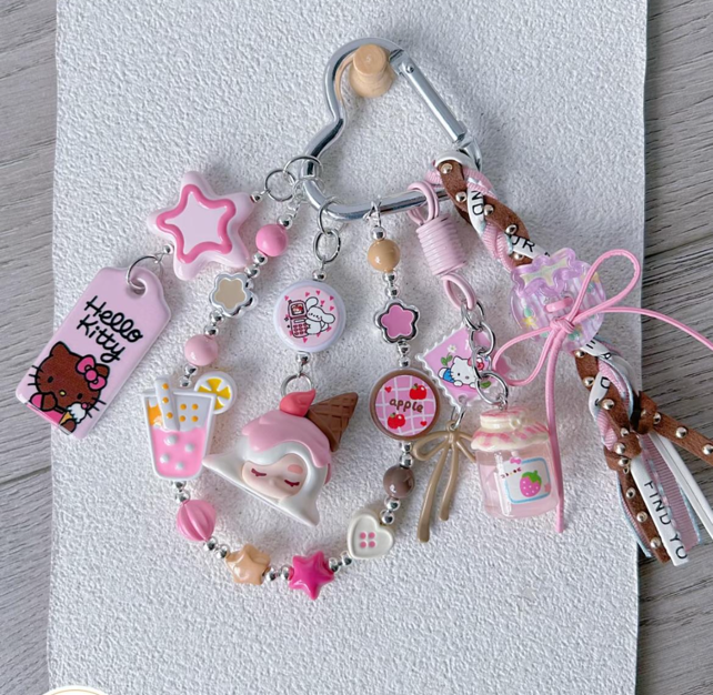 Decorative pink and brown hair clips with various cute charms, including Hello Kitty, a drink, ice cream cone, star, flower, and fruit charm, attached to a paperclip-style holder.