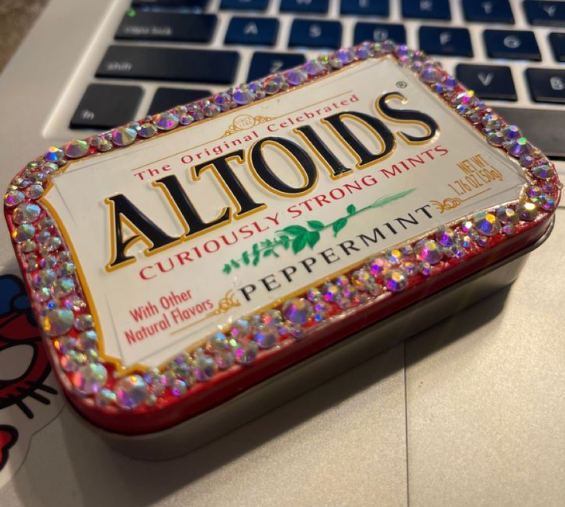 Decorative tin of Altoids peppermint mints with a rhinestone-encrusted border on a laptop keyboard.