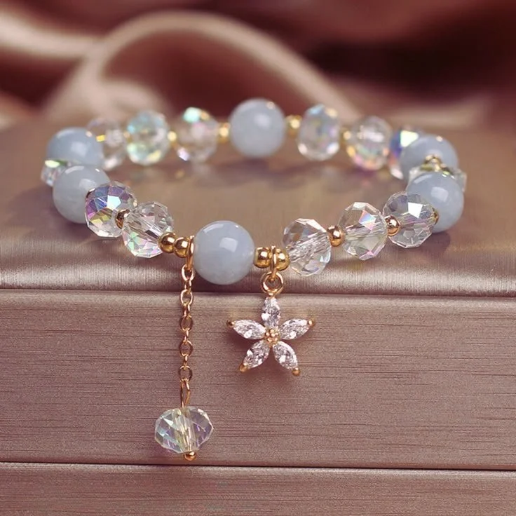 Gold and white beaded bracelet with crystal flower and heart charms on a satin surface.