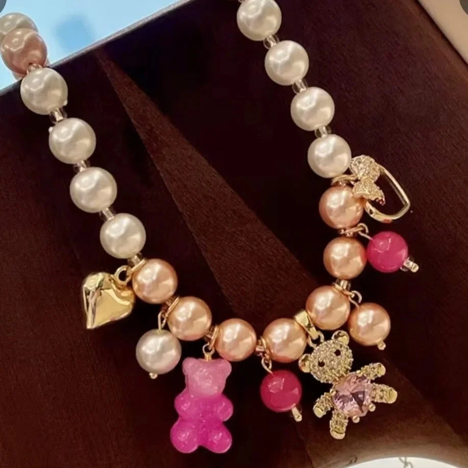 A pearl necklace with pink, gold, and pearl charms, including a pink teddy bear, a gold heart, a gold bear, and a pink bead.
