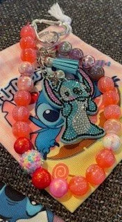 Colorful jewelry with a main charm of a blue unicorn from My Little Pony, surrounded by pink, orange, and multicolored round beads, resting on a surface with other items beneath.