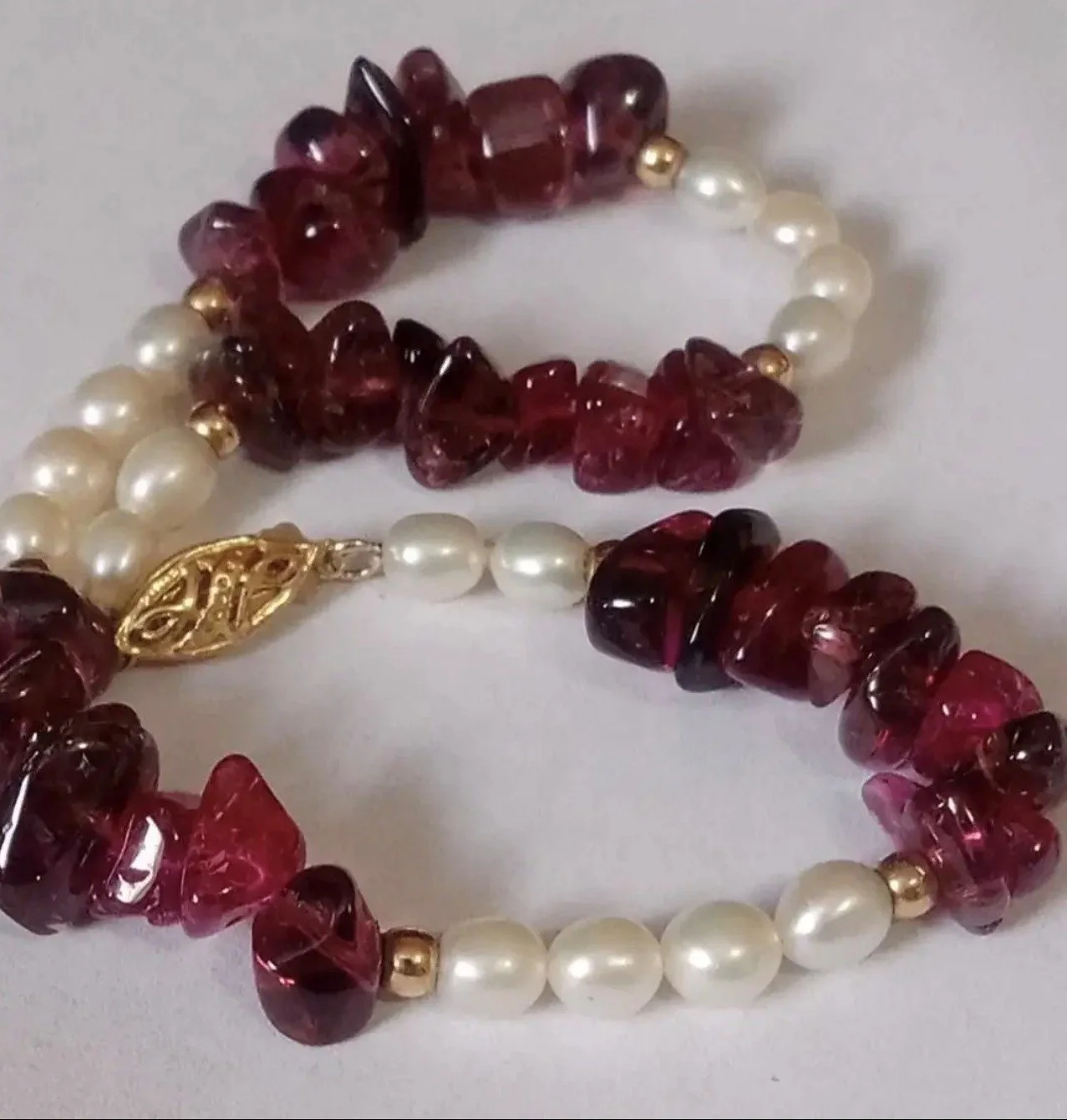 Close-up of a pearl and red gemstone necklace with a gold clasp on a white background.