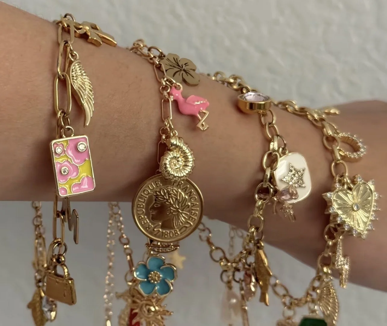 Multiple gold bracelets with 18K gold plated copper chains, and various styles of charms from enamel, to gold plated, gold alloy, various charms a feminine stackable collection