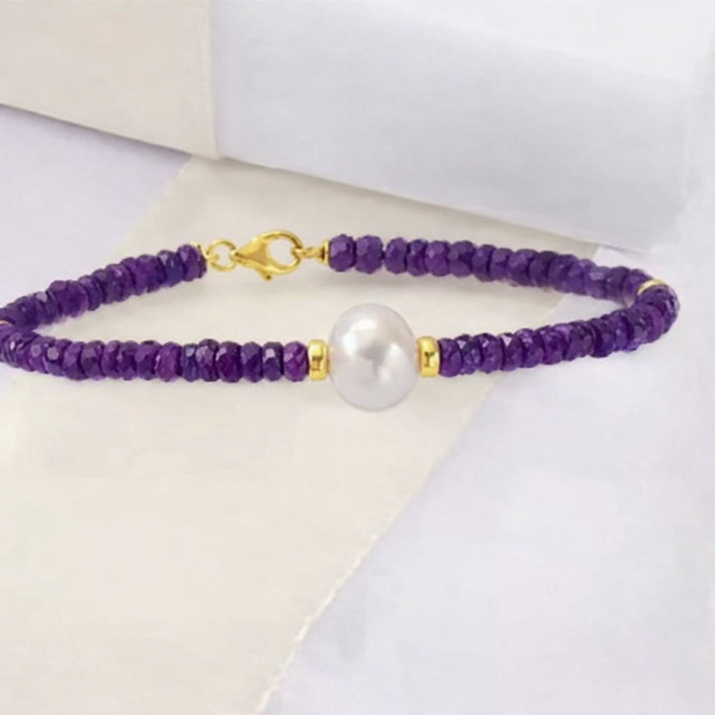 A purple beaded necklace with a large white pearl at the center, gold clasps, and small gold spacer beads, displayed on a white surface.