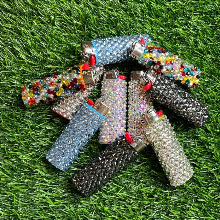 A collection of decorated lighters covered in rhinestones, arranged in a star pattern on artificial grass.