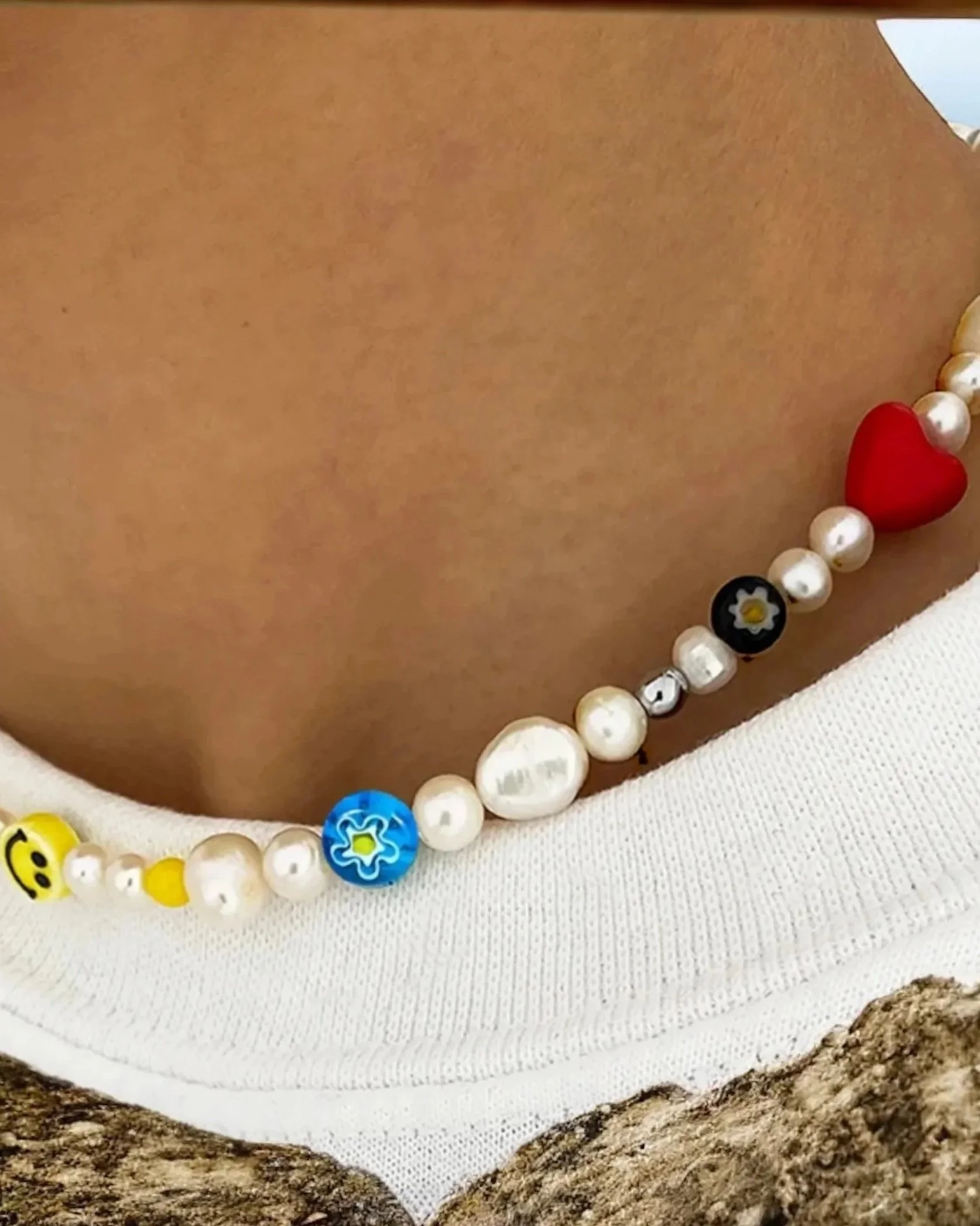 Close-up of a neckline with pearl and bead necklace including yellow, blue, and black beads, on a fabric surface.