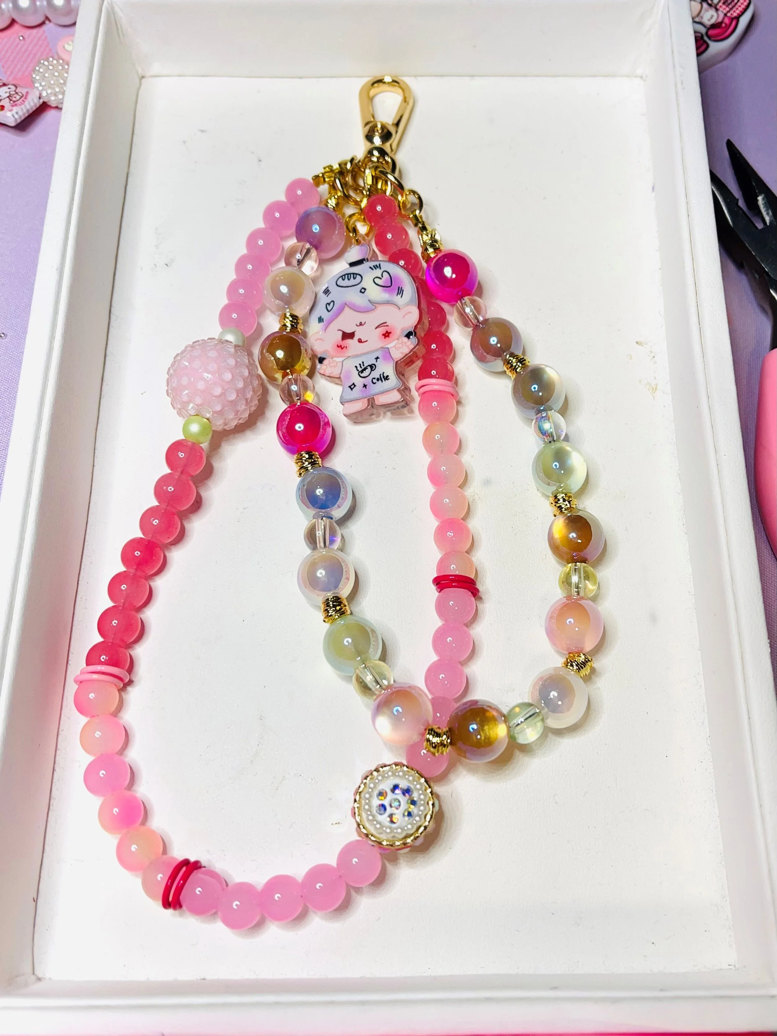 Pink and multicolored beaded necklaces with a cartoon character charm, inside a white jewelry box.