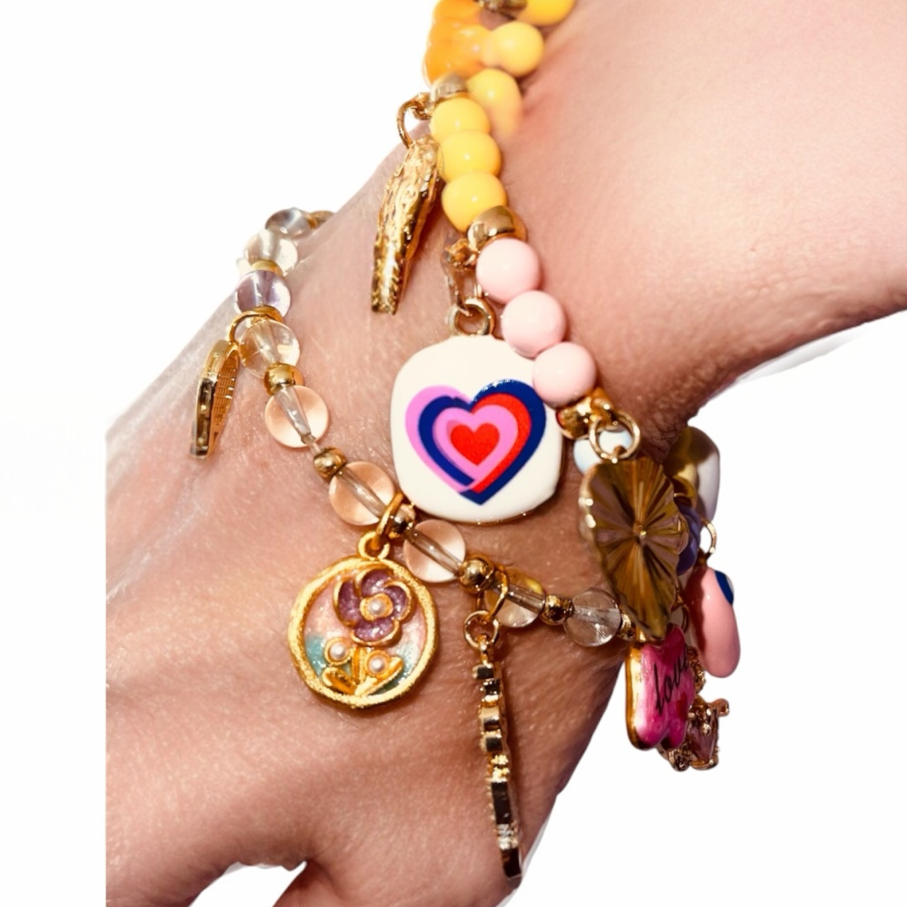 Multiple layered bracelets with charms, beads, and a colorful heart pendant on a person's wrist.
