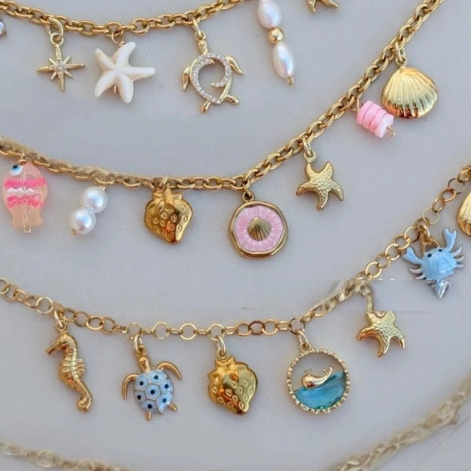 Gold necklaces with charms featuring seashells, starfish, crabs, seahorses, and other sea creatures, decorated with colorful enamel, beads, and pearls.