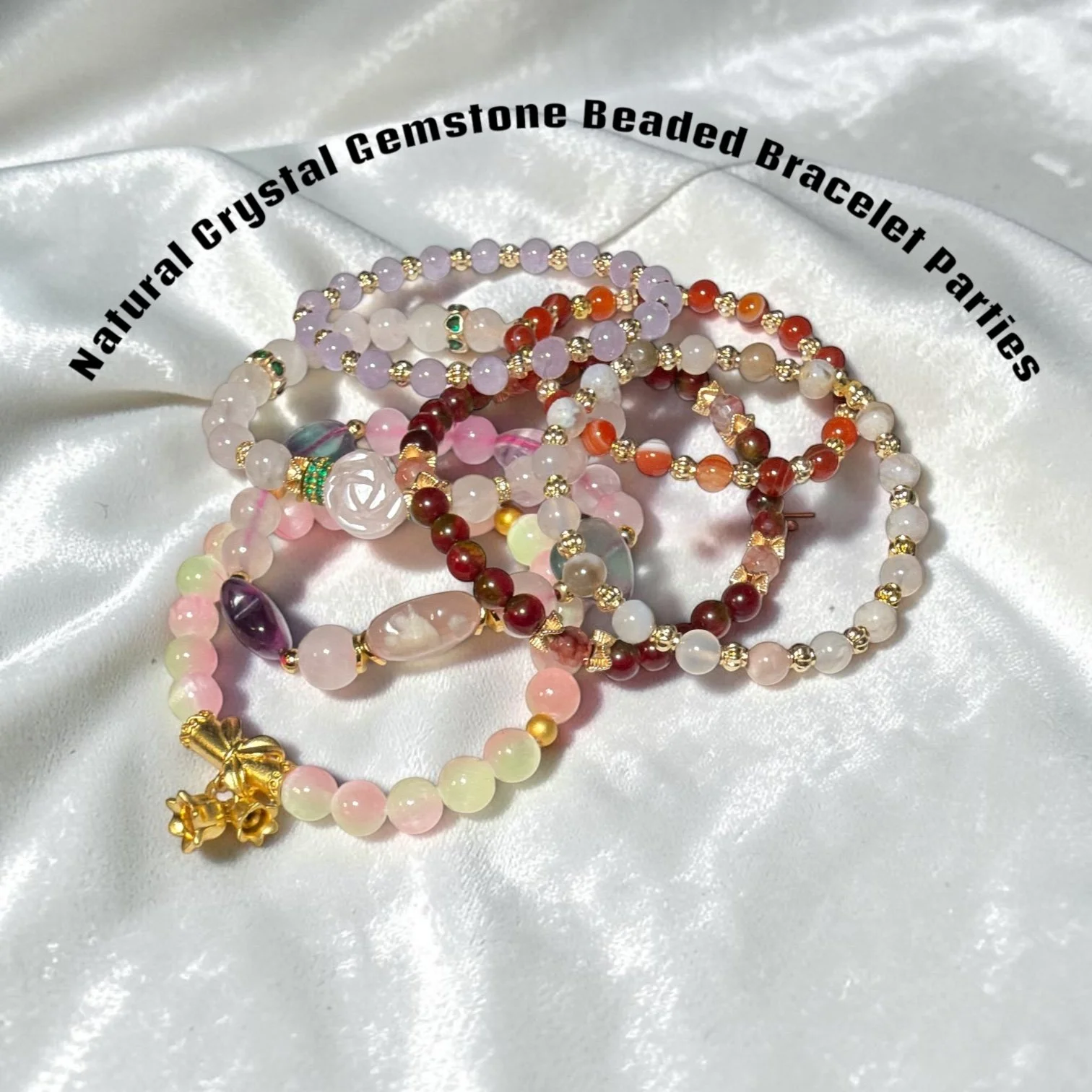 Several strands of colorful beaded jewelry, including bracelets and necklaces, lying on shiny white fabric. The beads are various colors and sizes, with some adorned with gold accents and charms.