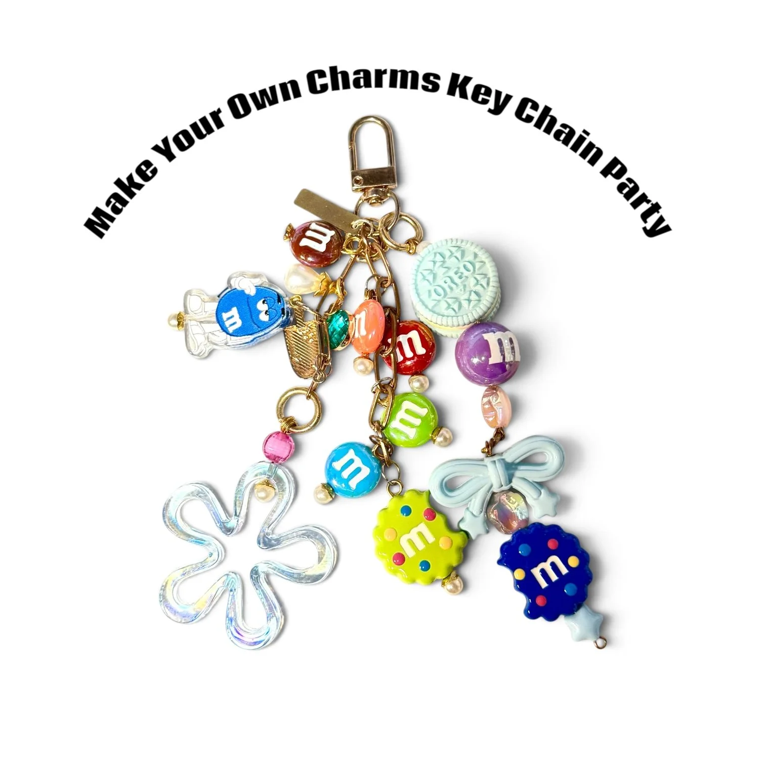 A collection of colorful key charms and accessories arranged in a circle with a metal clasp, including M&M's themed charms, a blue crystal flower, a yellow flower, bows, and assorted beads, with the phrase "Make Your Own Charms Key Chain Party" writt