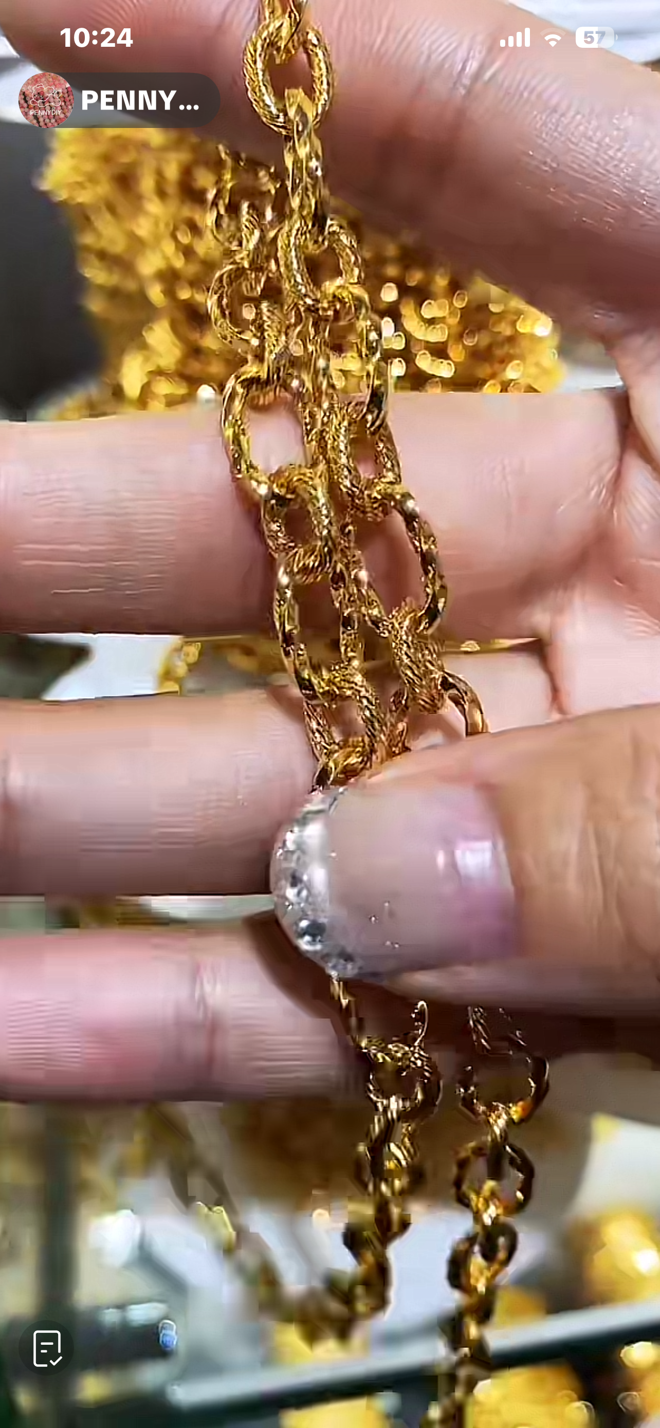 Close-up of a person's fingers holding a gold chain with a textured surface and a silver-colored ring with a large gemstone worn on the index finger.