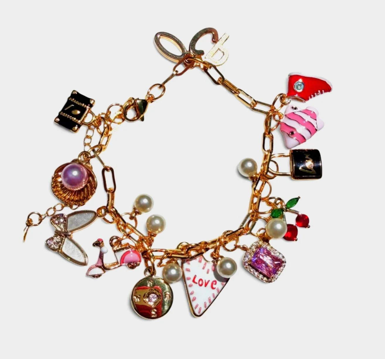 Gold charm bracelet with various colorful charms, including a pink heart with 'Love' written, a pearl, a butterfly, cherries, a shoe, a square with a diamond, a seashell, a black square with a 'V', a pink and white slice of cake, and other small deco